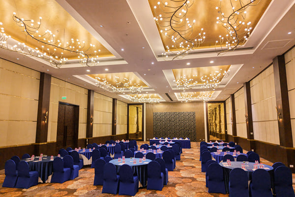 Panghat hall: large hall with round banquet tables, blue chairs and ornate lit ceiling chandeliers