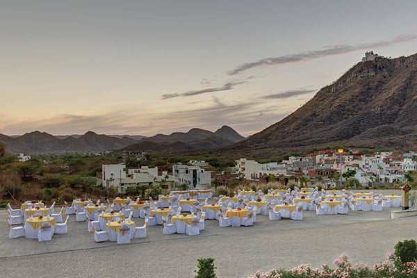 The resort: open terrace set with round tables and chairs at dusk beside hills and town