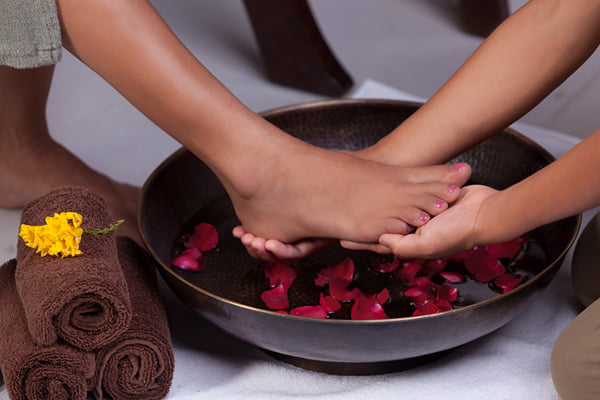 Sansha spa: hands washing feet in a bowl with rose petals beside rolled towels