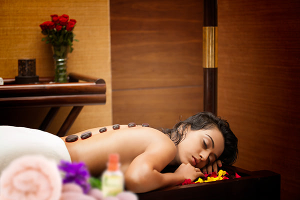 Sansha spa: woman lying face down with hot stones on her back, flowers and oil bottle nearby