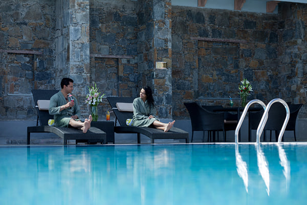 Sansha spa: couple in robes on loungers beside a pool with stone wall behind