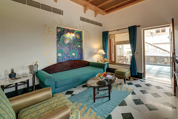 Suite: sitting area with teal sofa, peacock painting, armchair and balcony door