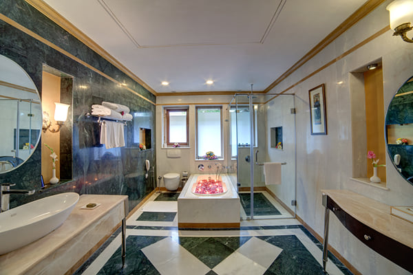 Suite: marble bathroom with vessel basin, tub with petals, glass shower and round mirrors