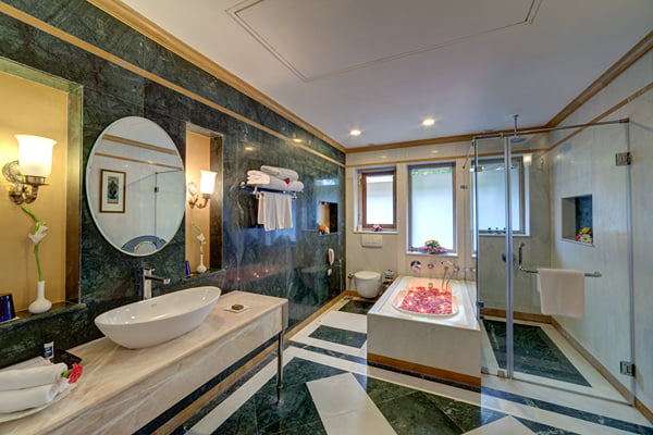 Suite: marble bathroom with vessel basin, petal-filled tub, glass shower and wall lights