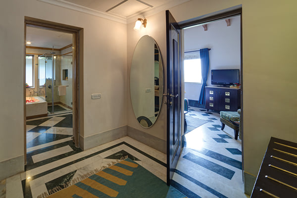 Suite: hallway with oval mirror and doorways to a bathroom and bedroom with TV