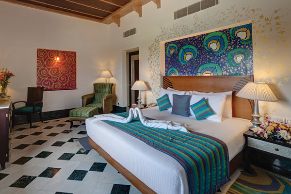 Suite: closer view of bed with striped runner, peacock artwork and green armchair