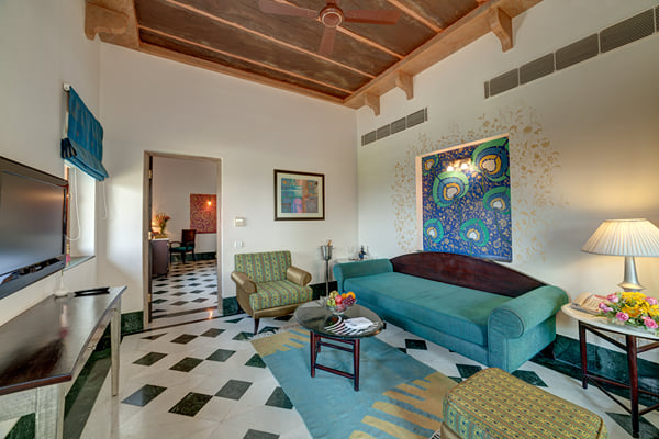 Suite: sitting room with teal sofa, peacock painting, armchair, television and ceiling fan