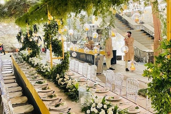 Wedding celebration: long banquet table with white flowers, clear chairs and hanging lanterns at night