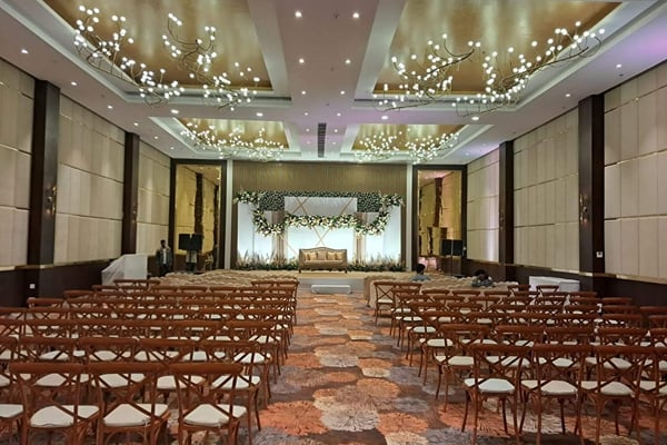 Wedding celebration: wide view of a ballroom with rows of wooden chairs facing a floral stage