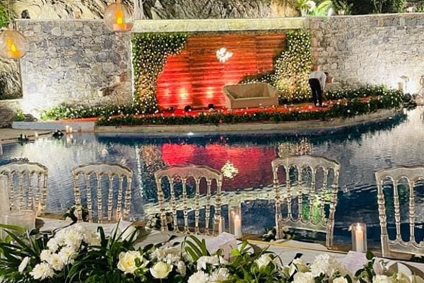 Wedding celebration: night wedding table with white flowers facing a pool with a red lit stage