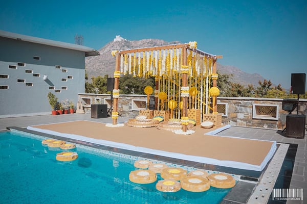 Wedding celebration: yellow flower-curtain mandap on platform over a pool with mountains behind