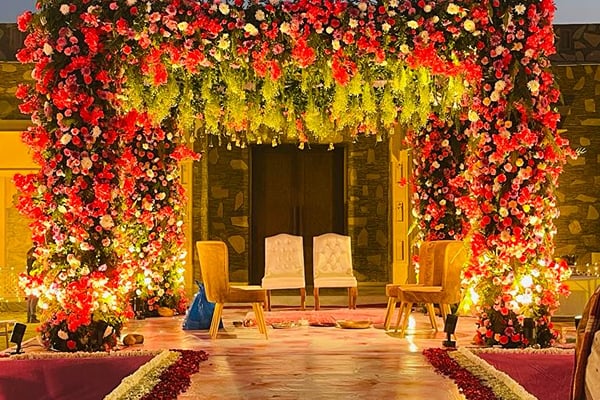 Wedding celebration: flower-covered gateway with chairs and lit pink carpet aisle at dusk
