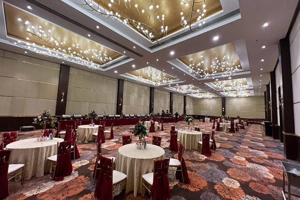 Wedding celebration: ballroom with round tables, burgundy chair covers and decorated ceiling chandeliers