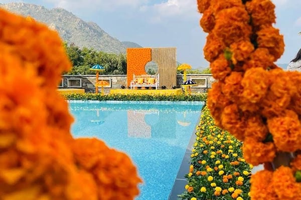 Wedding celebration: marigold garlands in foreground with pool and orange backdrop stage behind