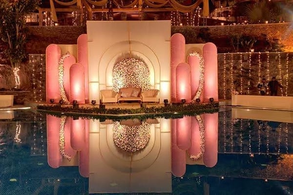 Wedding celebration: night view of pool with lit pink stage reflected in water and fairy lights