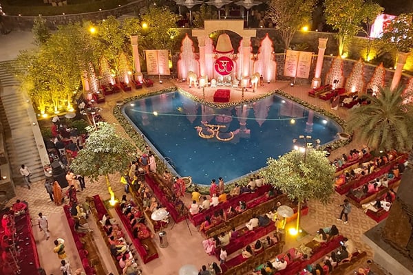 Wedding celebration: aerial view of pool with decorated stage and guests seated on red sofas at night