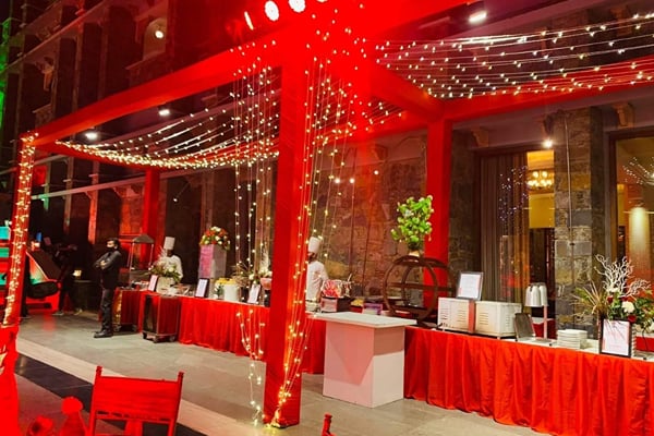 Wedding celebration: red-lit evening buffet counters under a canopy with string lights and chefs