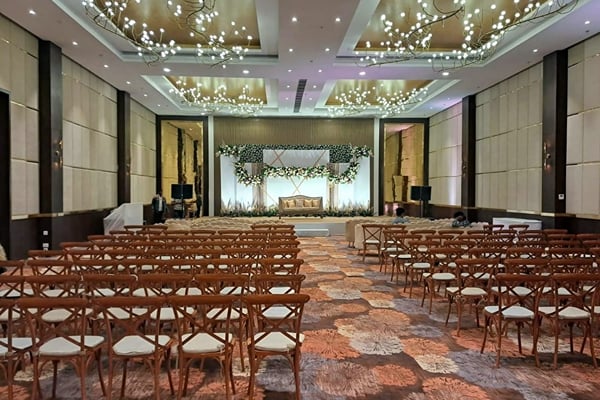 Wedding celebration: closer view of rows of wooden chairs facing a floral stage under chandeliers