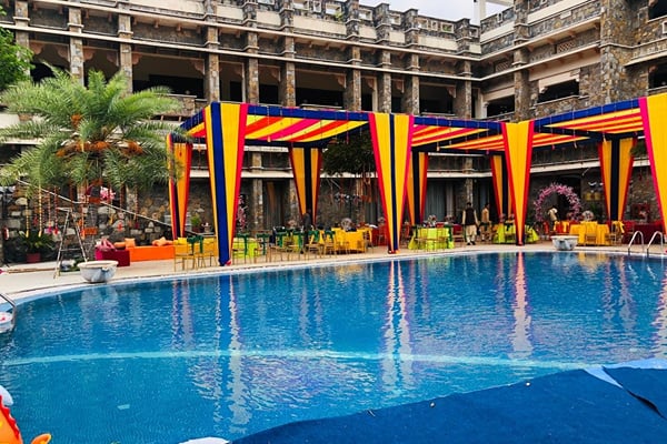 Wedding celebration: pool with striped blue, yellow and red canopies in front of stone resort building