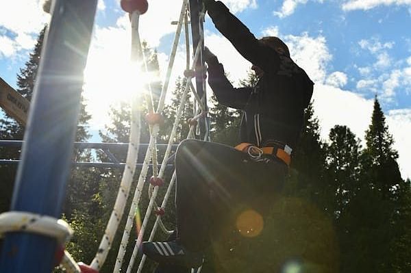 A low-angle view of a rope bridge or climbing structure against a bright sky.