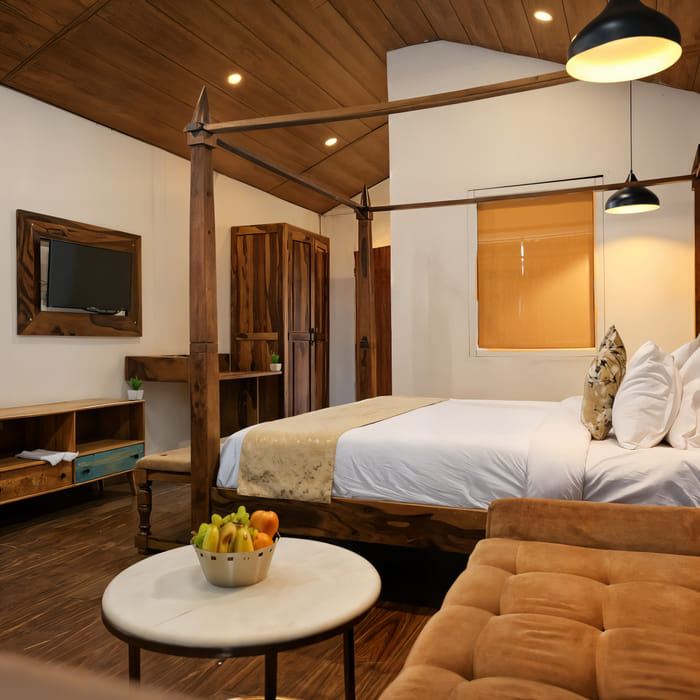Luxurious Cottage lounge area at Nazaara Nature Retreat, Dalhousie, with a cushioned armchair and wooden table by the window