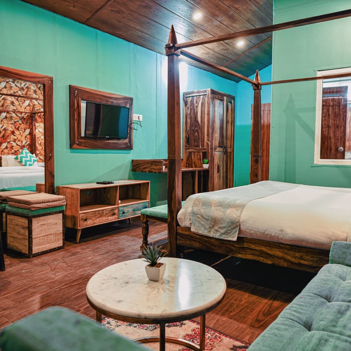 Bedroom lounge area of the Premium Cottage at Nazaara Nature Retreat, with teal armchairs and botanical wallpaper.