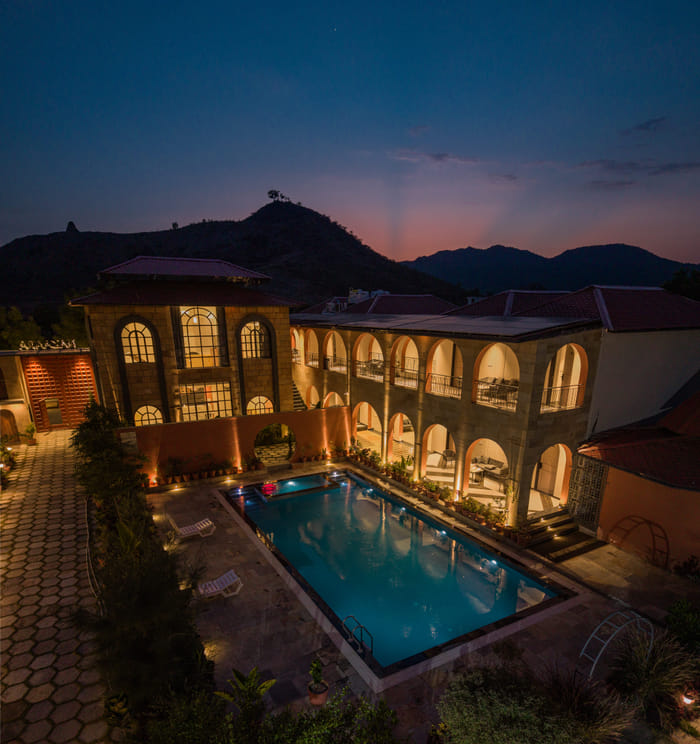 Nazaara Hills Retreat, Udaipur, aerial twilight view of the pool and surrounding hills