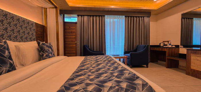 Bed, armchairs and a wall mirror in the Luxurious Room at Nazaara Luxe Retreat, Manali