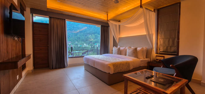 Canopy-draped king bed beside a large window in the Premium Room at Nazaara Luxe Retreat, Manali
