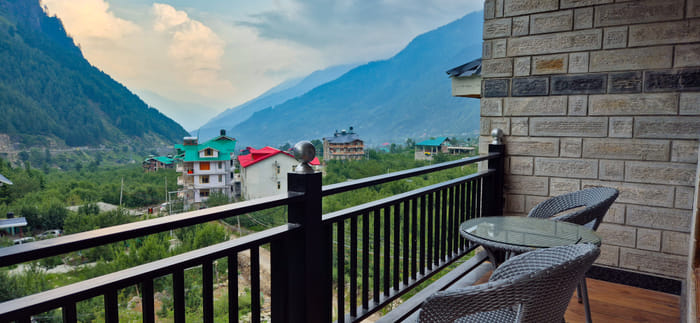 Private balcony of the Superior Room at Nazaara Luxe Retreat, cane chairs facing an open mountain view, Manali