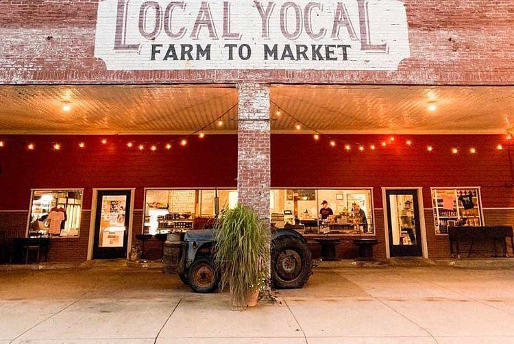 Exterior view of a market place named local yocal farm to market with a red wall on the outside and fairy lights as  decoration.