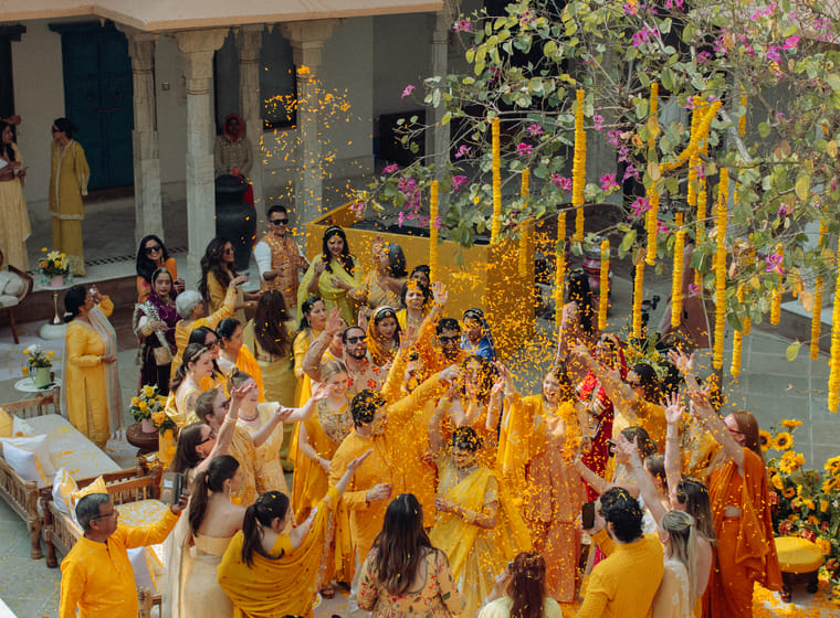 Wedding guests dressed in yellow toss flower petals during a haldi celebration in a marigold-draped heritage courtyard