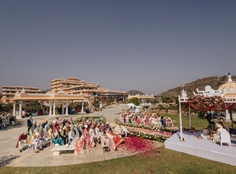 Guests gather on a garden lawn for an open-air wedding ceremony with the palace and hills behind
