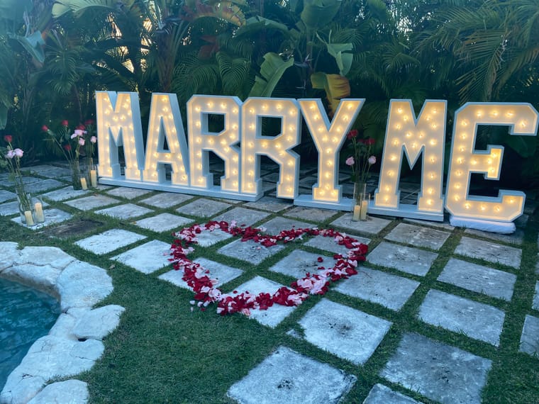 Illuminated MARRY ME letters and a heart of rose petals beside the pool at A Stone's Throw Away
