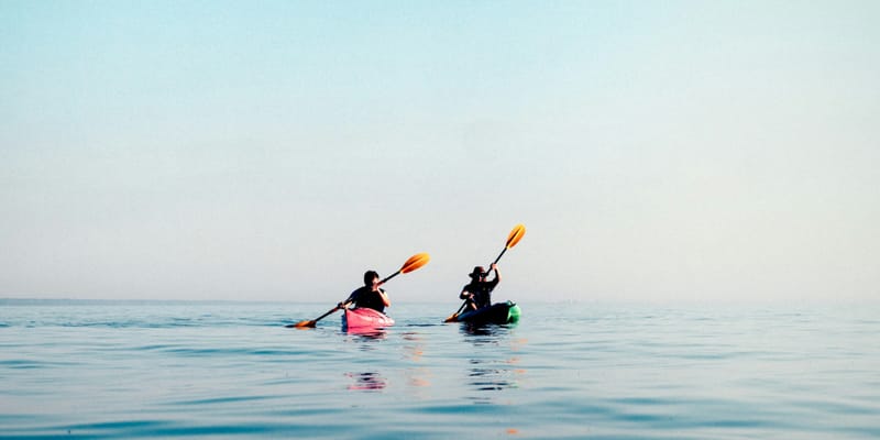 Two kayakers paddling on calm blue water at sunrise