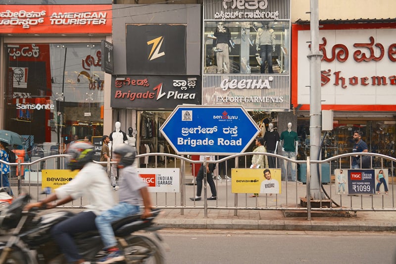 Brigade Road signboard and shopfronts with traffic on the street