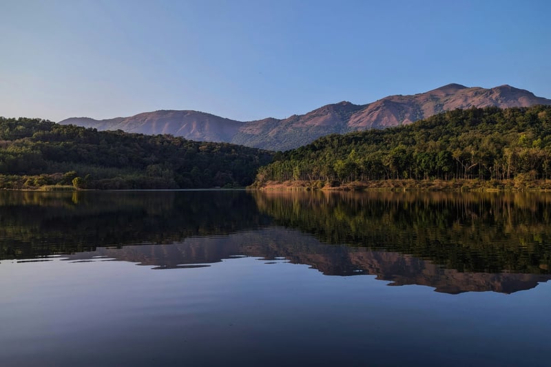Still waters of Hirekolale Lake reflecting forested hills at dusk