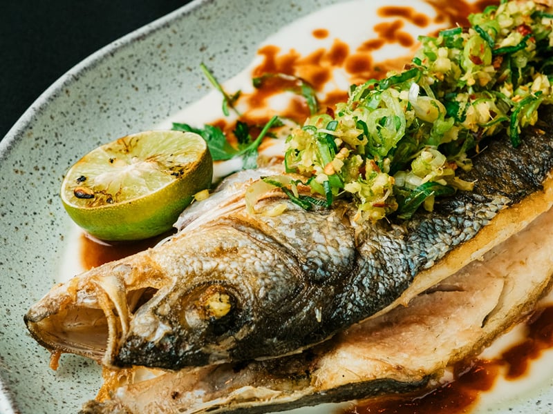 Whole grilled fish on a ceramic plate with lime, fresh herbs, and a dark sauce | Shirgaonkar Beach Resort