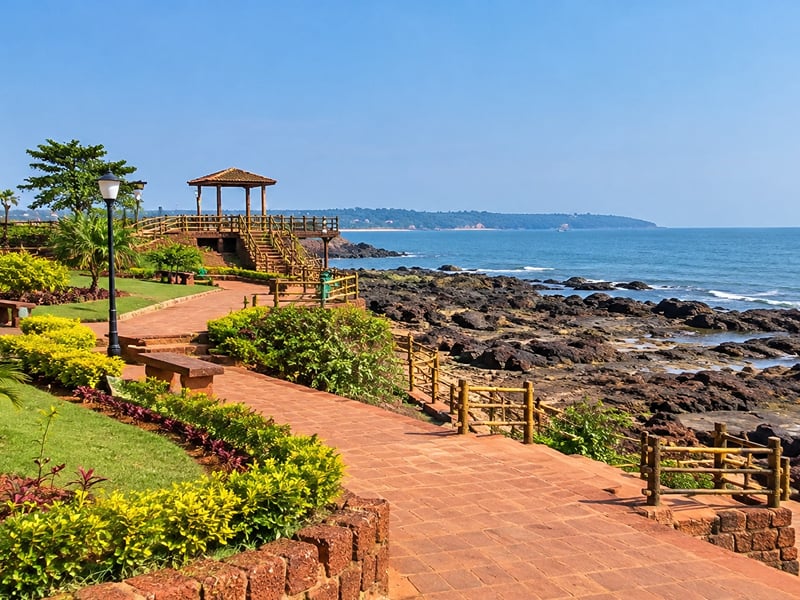 Paved path curving past clipped shrubs to a wooden gazebo above the rocky shore | Shirgaonkar Beach Resort