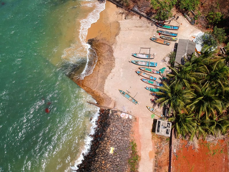 Aerial view of a curved beach with fishing boats drawn up on the sand and coconut palms behind | Shirgaonkar Beach Resort