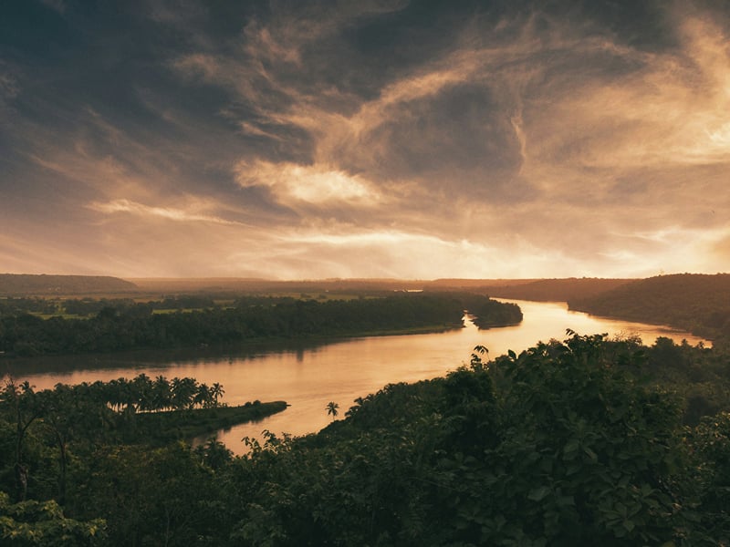 River winding out to the sea through dense green, under a gold and grey evening sky | Shirgaonkar Beach Resort
