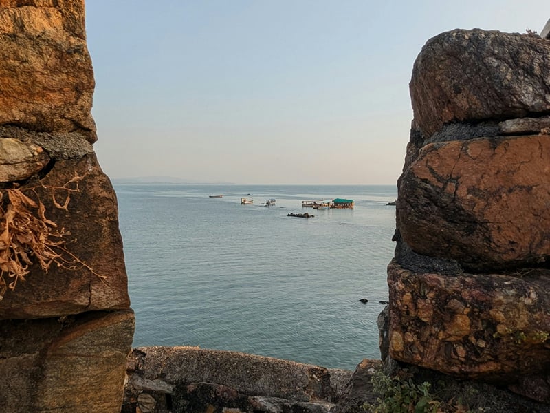 Boats on the open sea framed by a gap in the stone ramparts of Sindhudurg Fort | Shirgaonkar Beach Resort