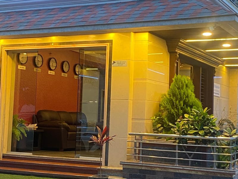 Brightly lit entrance of Value Inn, Bangalore Airport at night with a glowing blue name board, warm lighting, and potted plants by the door