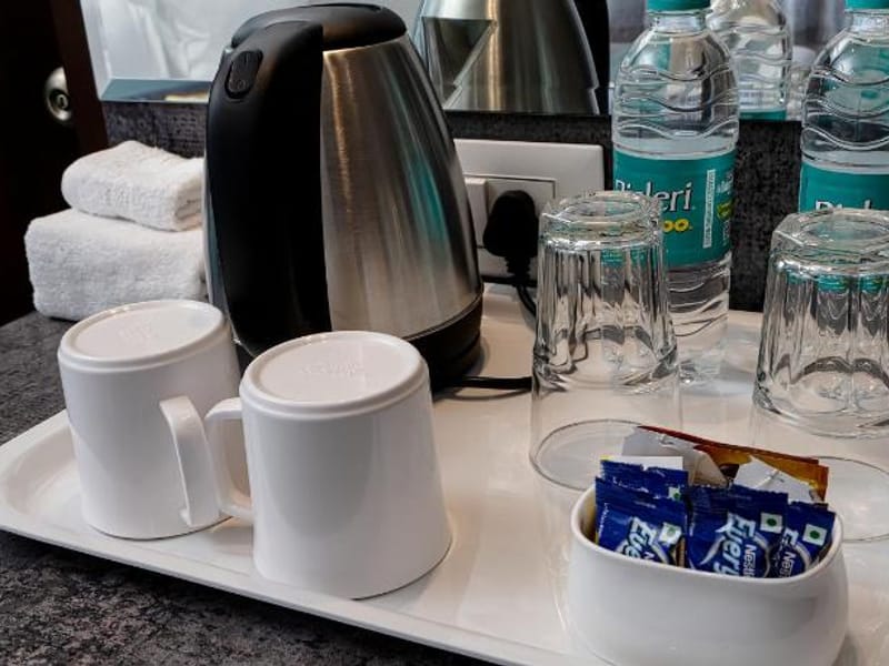 Tea and coffee tray at Value Inn, Bangalore Airport with an electric kettle, cups, glasses, biscuit sachets, and bottles of mineral water