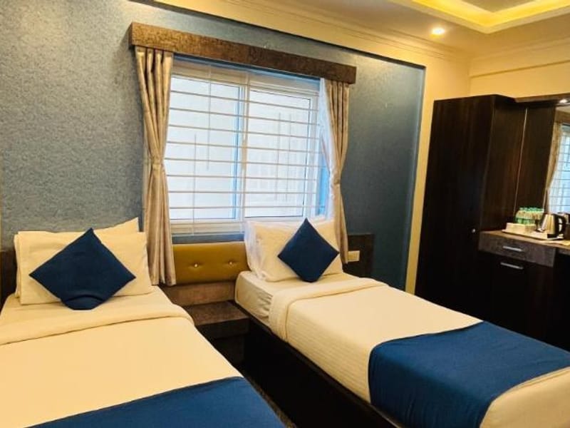 2 single beds with blue cushions and runners beside a bright window in the Standard AC Twin Room at Value Inn, Bangalore Airport