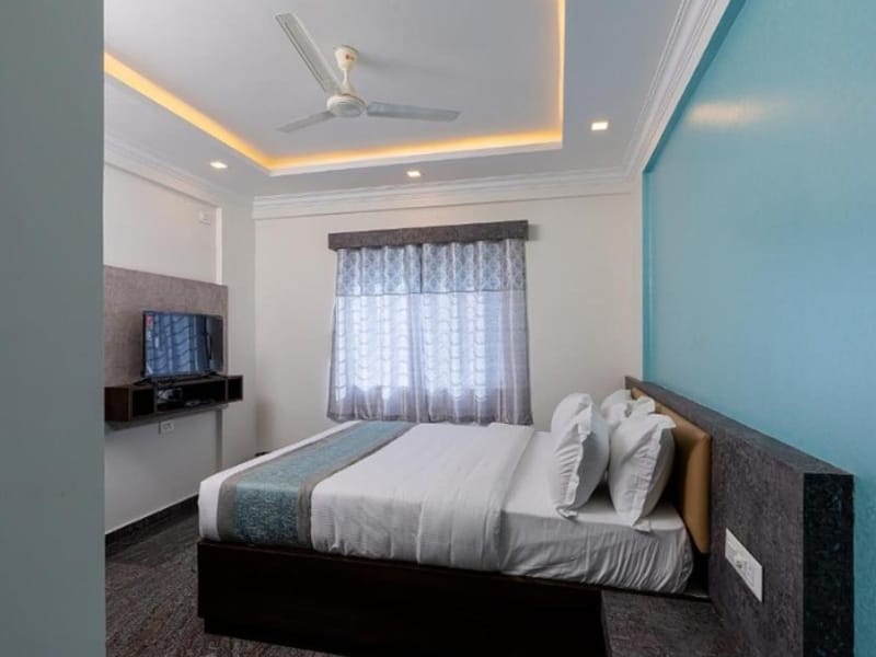 Standard Non-AC Room at Value Inn, Bangalore Airport with a queen bed, teal feature wall, ceiling fan, cove lighting, and a bright window