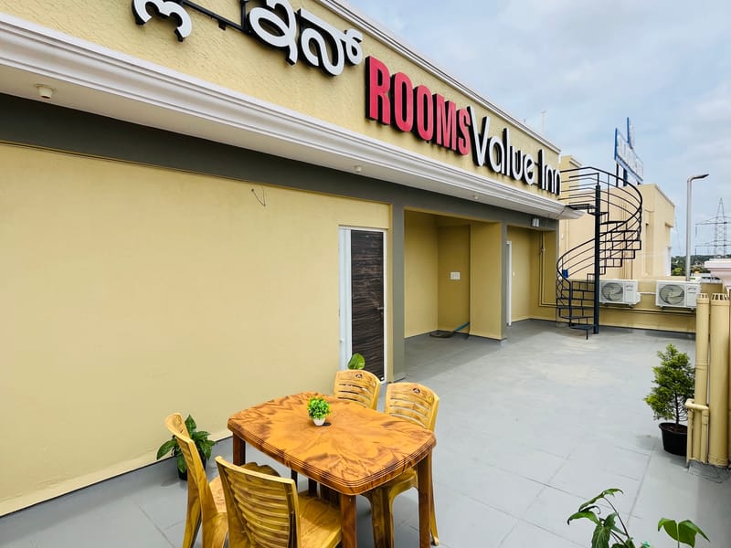Wooden dining table and chairs on the rooftop terrace at Value Inn, Bangalore Airport beside the hotel signage and potted green plants