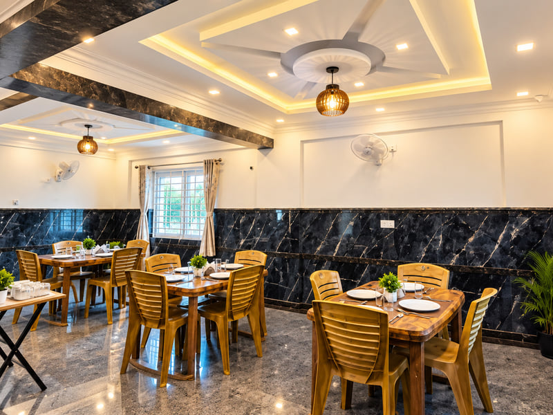 Dining area at Value Inn, Bangalore Airport with wooden tables set for a meal, black marble walls, pendant lamps, and a warmly lit tray ceiling