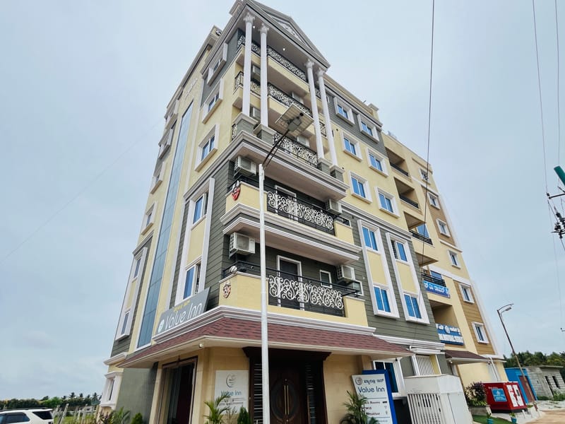 Side angle of the Value Inn, Bangalore Airport building showing its cream and grey exterior, balconies, and open surroundings in Yelahanka
