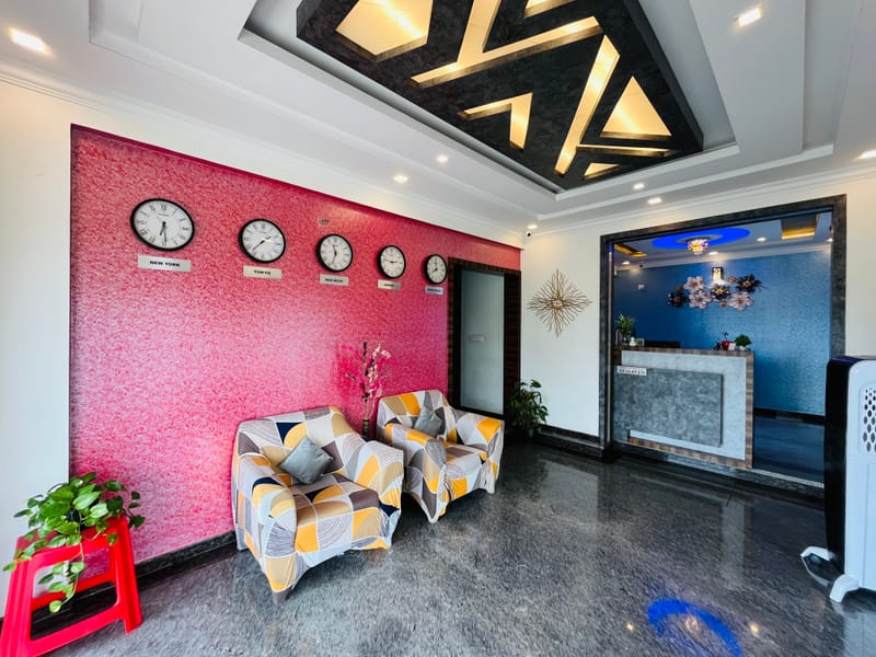 Lobby seating at Value Inn, Bangalore Airport with a patterned sofa, world clocks on a red feature wall, and the reception counter behind
